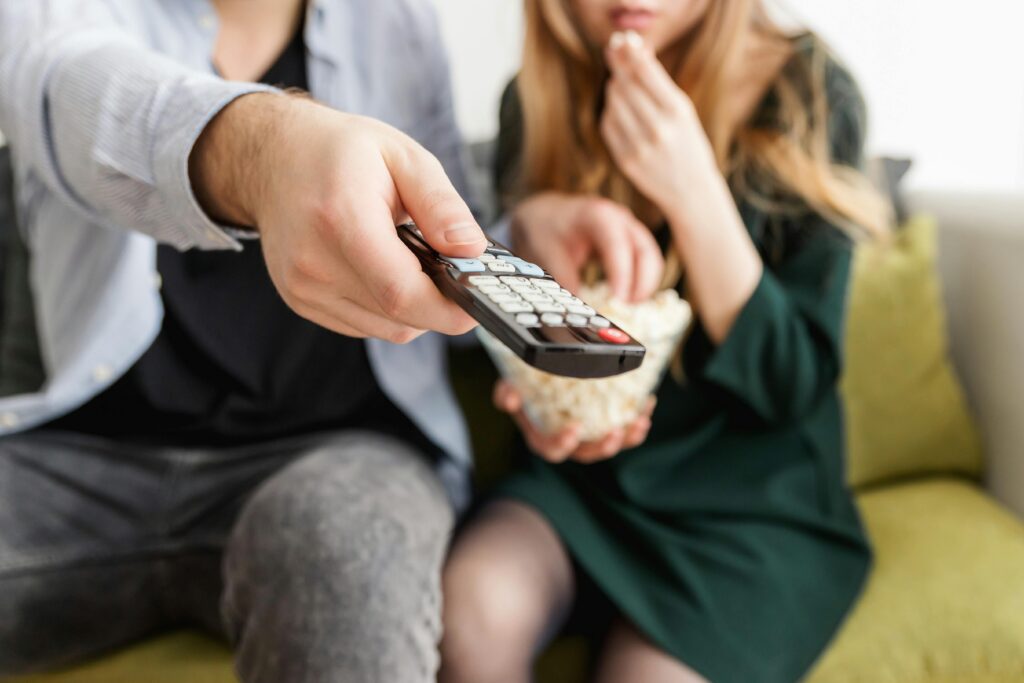 A couple enjoying a relaxing movie night, sitting on a sofa with popcorn and a TV remote. Smart TV
