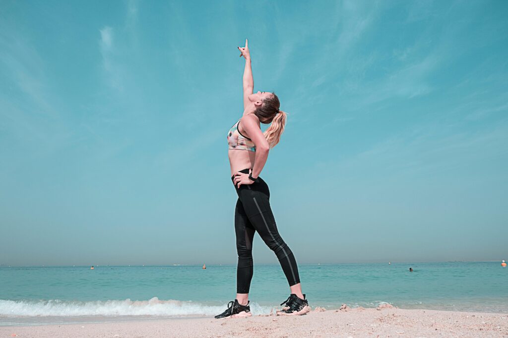 A woman performing a stretching exercise on a sunny beach in Dubai. best supplements 2025