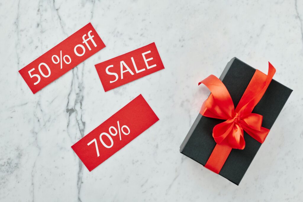 Stylish black gift box with red ribbon and sale tags on marble, perfect for Black Friday promotions. Cupons