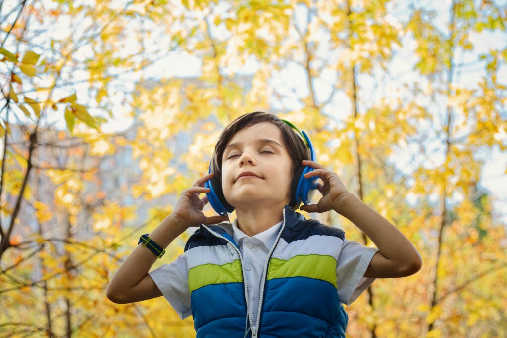 A young boy enjoys music through headphones amidst colorful fall foliage. Best Headphones