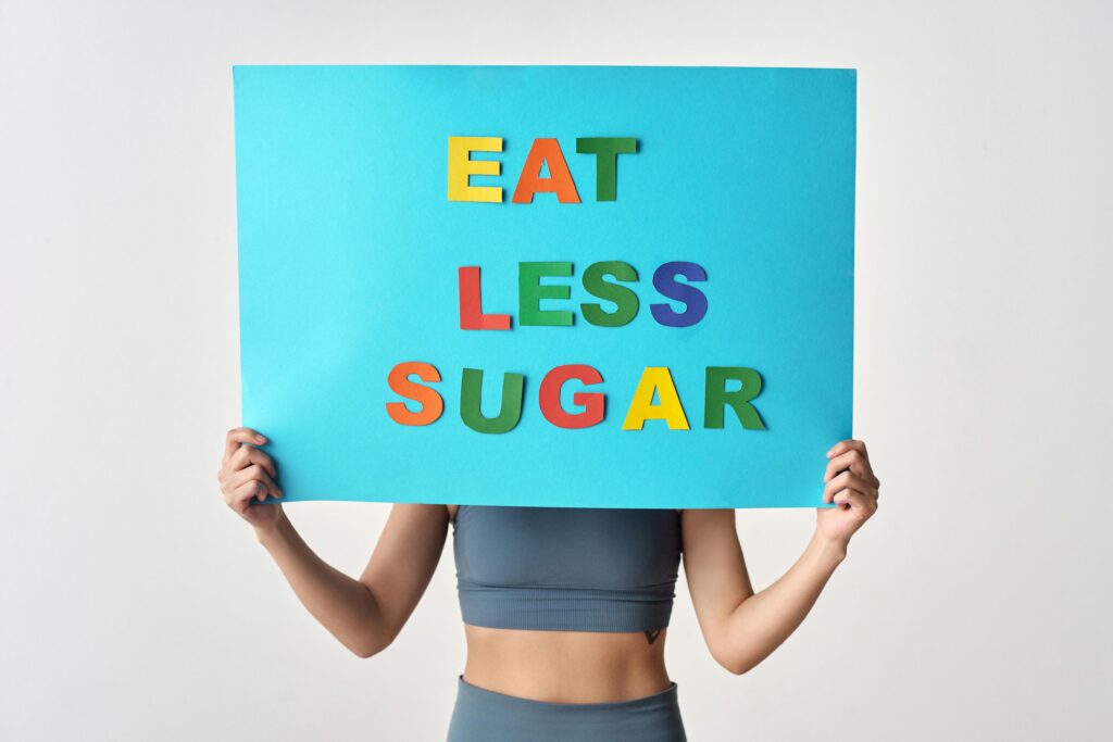 Woman holding colorful 'Eat Less Sugar' sign on white background promoting health awareness.