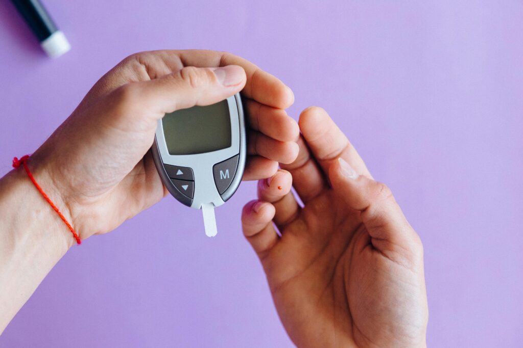 Hands holding a glucometer to test blood sugar levels on a purple background.Free Sugar Pro